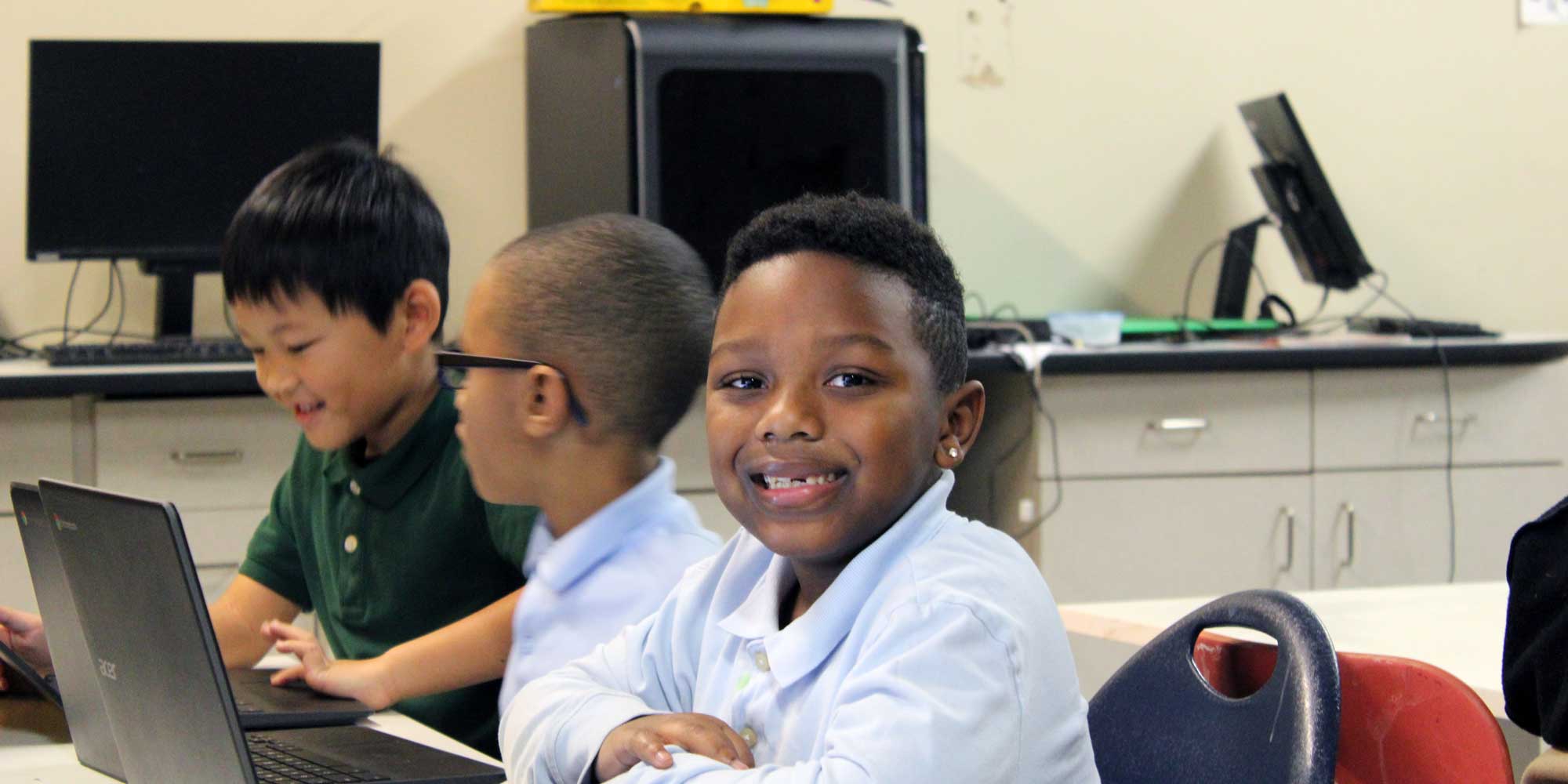 Students working on laptops at a classroom table.